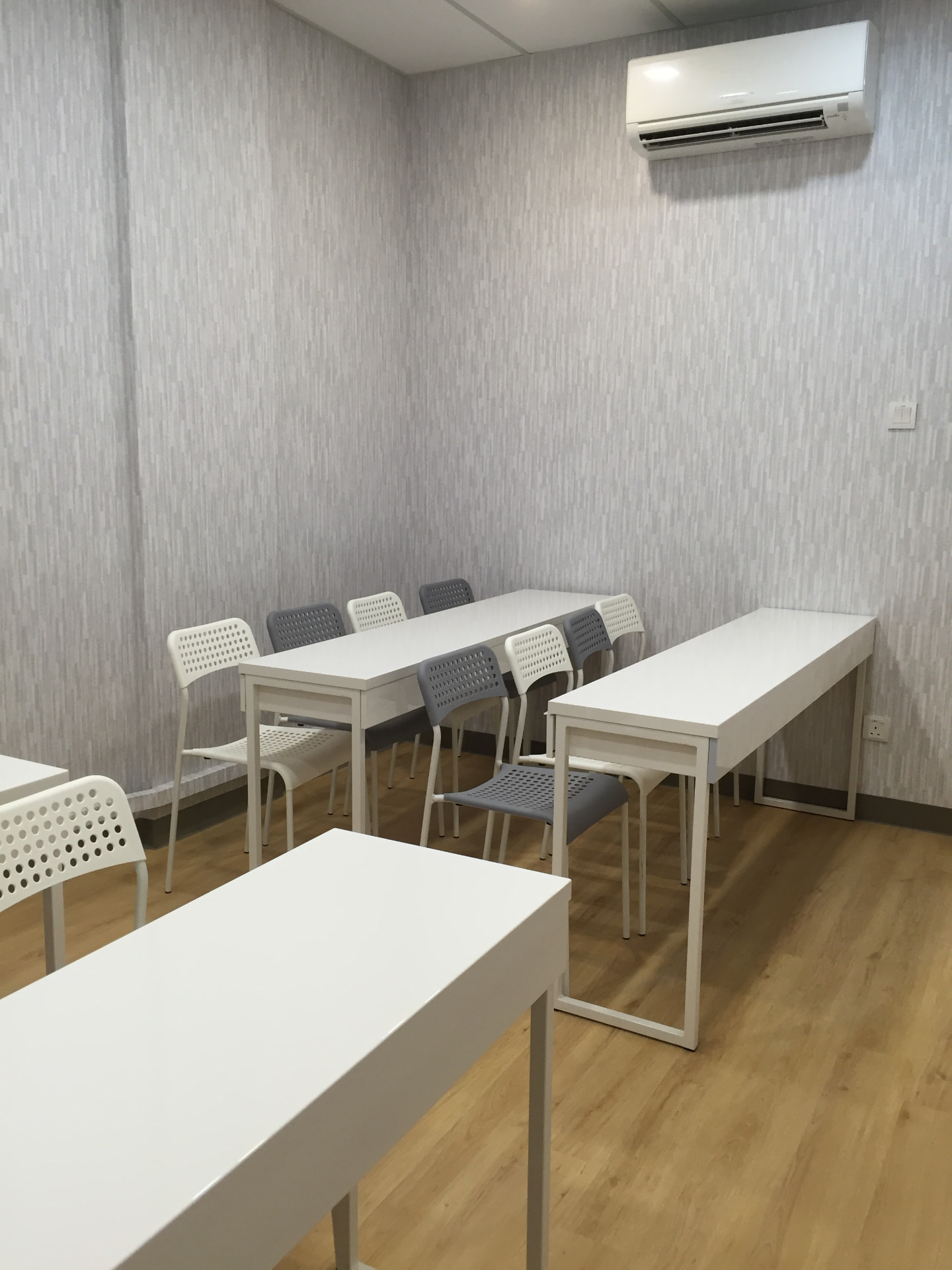 Small AZKEN class room with two rows of white tables and grey chairs