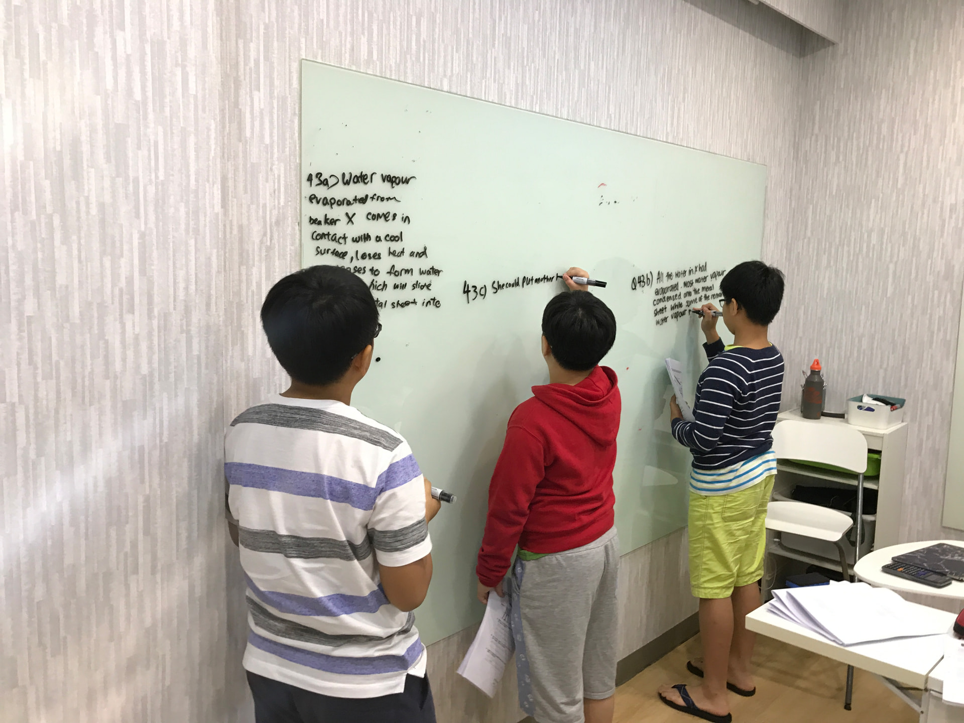 Three AZKEN students writing their answers on a whiteboard during a small-group lesson